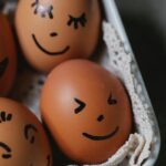 From above of brown chicken eggs with different painted funny faces placed in ceramic dish in kitchen