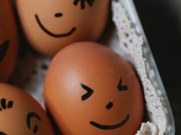 From above of brown chicken eggs with different painted funny faces placed in ceramic dish in kitchen