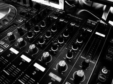 Black and white close-up of a DJ's audio mixing console with knobs and controls.