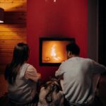 A couple and their dog enjoying a warm evening by the fireplace indoors.