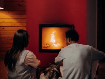 A couple and their dog enjoying a warm evening by the fireplace indoors.