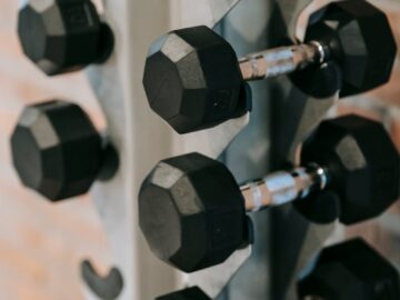 Close-up of black dumbbells on a rack in a contemporary gym with a brick wall backdrop.