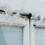 Sharp icicles hang from a window frame, covered in snow, showcasing winter's beauty.