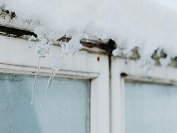 Sharp icicles hang from a window frame, covered in snow, showcasing winter's beauty.