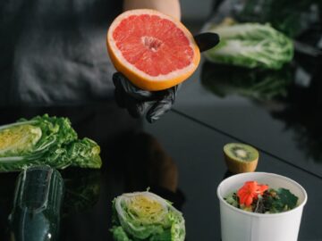 Person preparing a healthy meal with fresh grapefruit, kiwi, and lettuce.