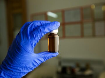 Unrecognizable doctor wearing glove standing in room with glass bottle of vaccine for injection on blurred background during coronavirus pandemic