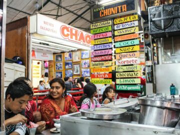 A lively Mexican ice cream shop with colorful signs and diverse customers enjoying treats.