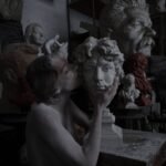 Creative sculptor in a cluttered studio with various busts.