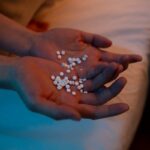 A person holding a handful of pills in a dimly lit bedroom, conveying themes of health and mental wellness.