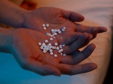 A person holding a handful of pills in a dimly lit bedroom, conveying themes of health and mental wellness.