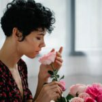 A woman gently smelling pink roses indoors, creating a serene and floral ambiance.