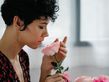 A woman gently smelling pink roses indoors, creating a serene and floral ambiance.