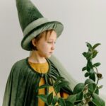 A child dressed as a wizard holding a plant, evoking fantasy and magic.