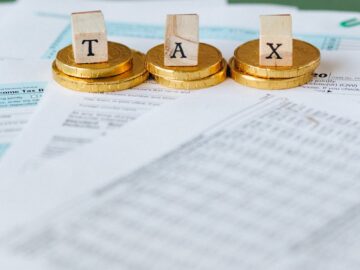 Staged image of gold coins with tax letter tiles on documents.