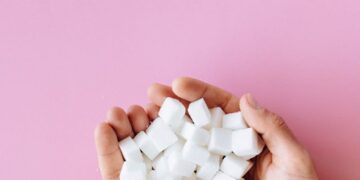 Open hands holding sugar cubes against a vibrant pink surface, symbolizing sweetness and health awareness.