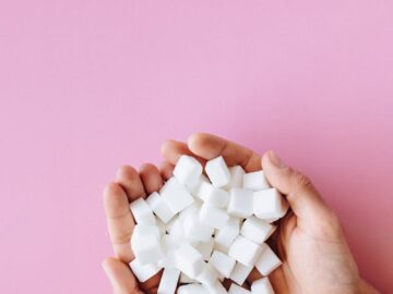 Open hands holding sugar cubes against a vibrant pink surface, symbolizing sweetness and health awareness.