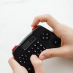 Close-up of hands holding a small, black electronic calculator with a digital display.