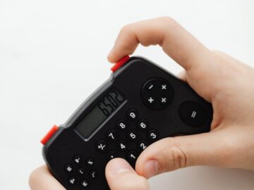 Close-up of hands holding a small, black electronic calculator with a digital display.