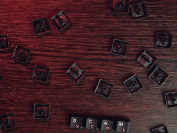 Scattered keyboard keys spelling 'SCAM' on a red-lit wooden surface, symbolizing online fraud.