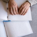 Hands reading Braille text on an open book, representing tactile reading and accessibility.