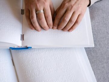 Hands reading Braille text on an open book, representing tactile reading and accessibility.