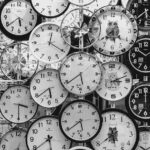 A black and white image displaying a diverse array of vintage wall clocks.
