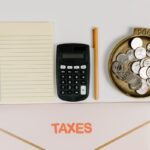 Flat lay of tax preparation tools including a calculator, notebook, and coins.