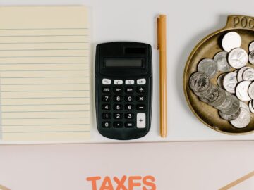 Flat lay of tax preparation tools including a calculator, notebook, and coins.