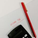 Close-up of a calculator and red pen on paper labeled 'Income Tax', representing financial planning.