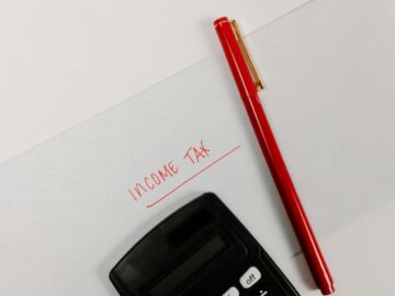 Close-up of a calculator and red pen on paper labeled 'Income Tax', representing financial planning.