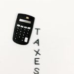 Black calculator and letter tiles spelling 'TAXES' on a smooth white background, symbolizing financial calculations.