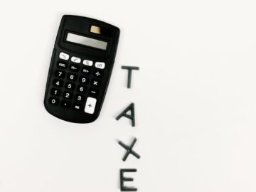 Black calculator and letter tiles spelling 'TAXES' on a smooth white background, symbolizing financial calculations.