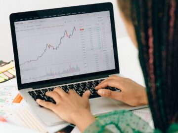 A woman working on financial analysis using a laptop with a stock market graph on screen.