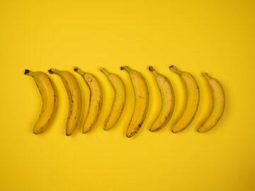 Top view of tasty ripe bananas with blots on peel composed in row on yellow background