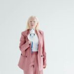Portrait of a confident woman in a pink suit holding a megaphone on a white background, promoting leadership and empowerment.