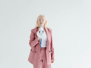 Portrait of a confident woman in a pink suit holding a megaphone on a white background, promoting leadership and empowerment.