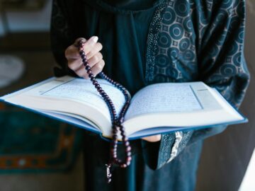 A woman in traditional attire reads a holy book with prayer beads, symbolizing faith and devotion.