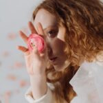 Artistic portrait of a redheaded woman holding a pink flower over one eye.