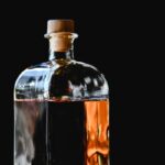 A stylish glass bottle of whiskey with cork stopper against a dramatic black backdrop.