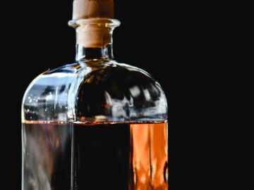 A stylish glass bottle of whiskey with cork stopper against a dramatic black backdrop.