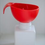 A red funnel placed on an empty white bottle against a plain backdrop. Ideal for product mockups.