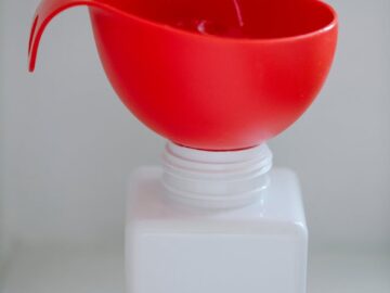 A red funnel placed on an empty white bottle against a plain backdrop. Ideal for product mockups.