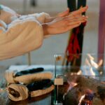 Close-up of hands warming by a fire outdoors in winter. Gloves on the table suggest a cold day.
