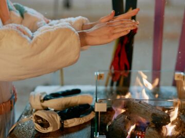 Close-up of hands warming by a fire outdoors in winter. Gloves on the table suggest a cold day.