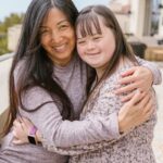 A joyful moment of a mother and daughter with Down syndrome sharing a warm embrace outdoors.