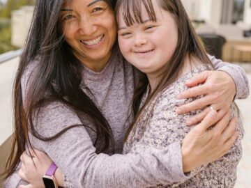 A joyful moment of a mother and daughter with Down syndrome sharing a warm embrace outdoors.