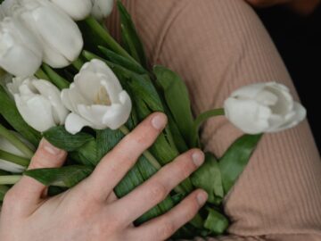 Close-up of diverse hands holding a bouquet of white tulips in a warm embrace.