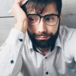 Portrait of a distressed man with glasses holding a paper, looking worried indoors.