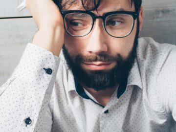 Portrait of a distressed man with glasses holding a paper, looking worried indoors.