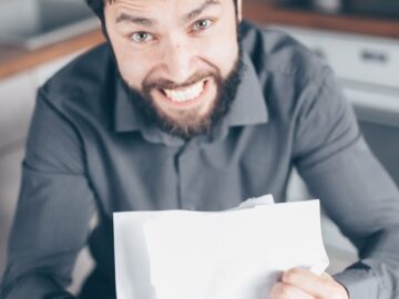 A frustrated man holding papers in a kitchen, showing stress and anxiety.